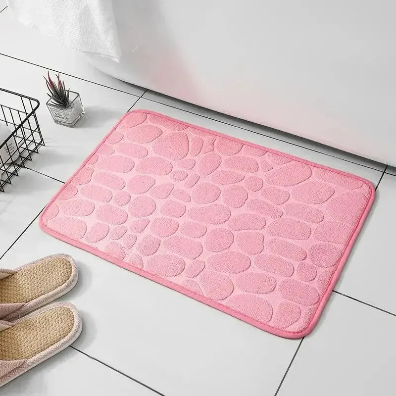 GLOBGRIP pink anti slip pebble floor mat placed on white tiled floor with slippers nearby