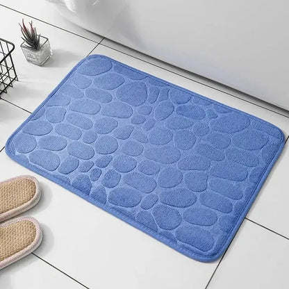 GLOBGRIP anti slip pebble floor mat in blue placed on white tiled floor with slippers nearby