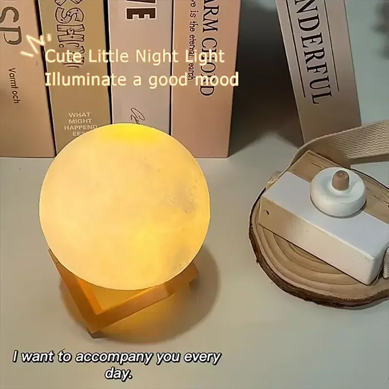GLOBGRIP Book Light LED Moon Galaxy Night Light glowing with warm yellow light on a desk with books
